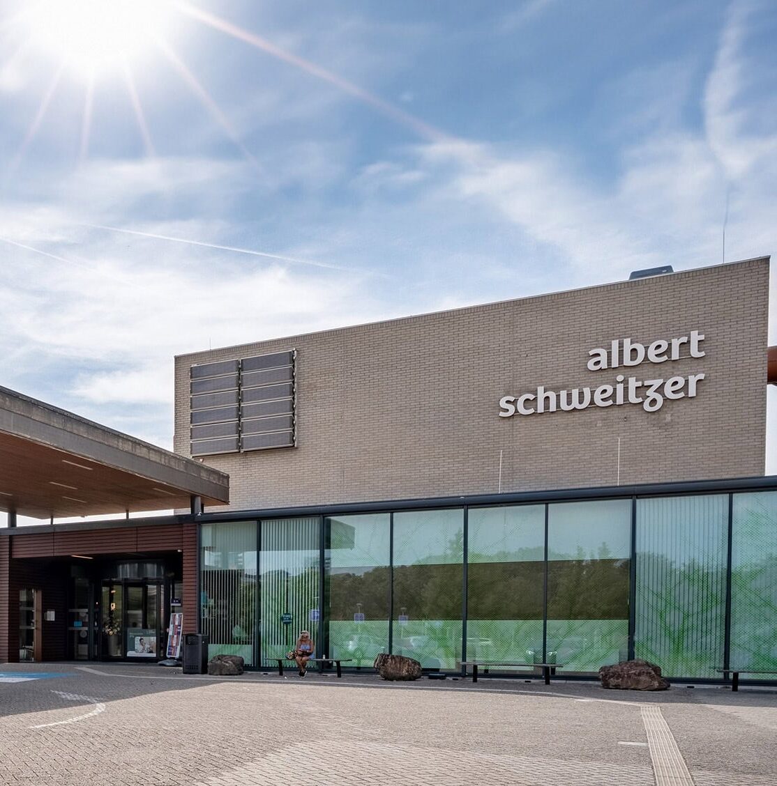 Image of the front and entrance of the Helene Schweitzer Clinic. The façade displays the words “Alber Schweitzer” in large letters, and the building features large windows that allow natural daylight to enter.